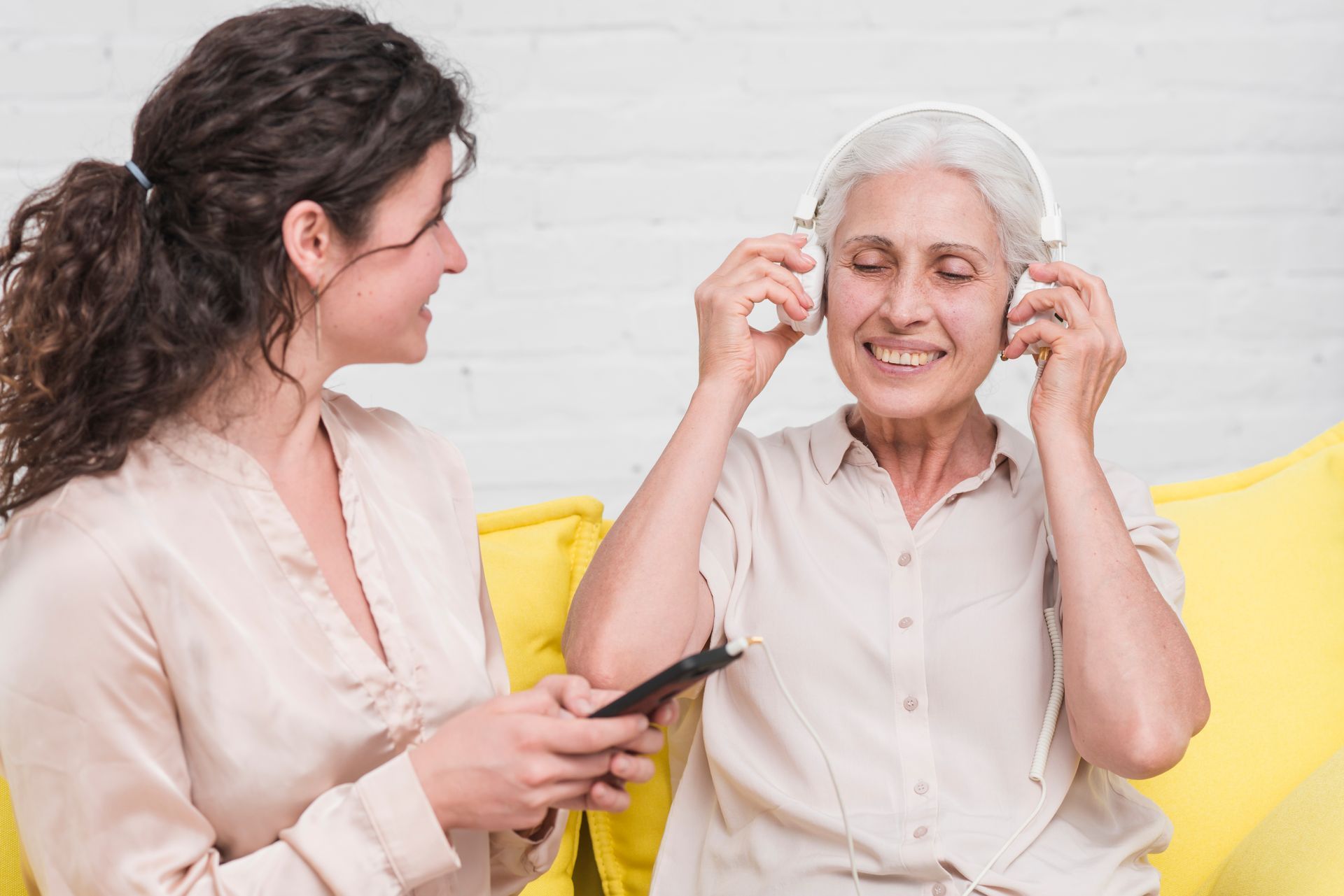 Woman helping older woman put on headphones; both smiling, indoors.