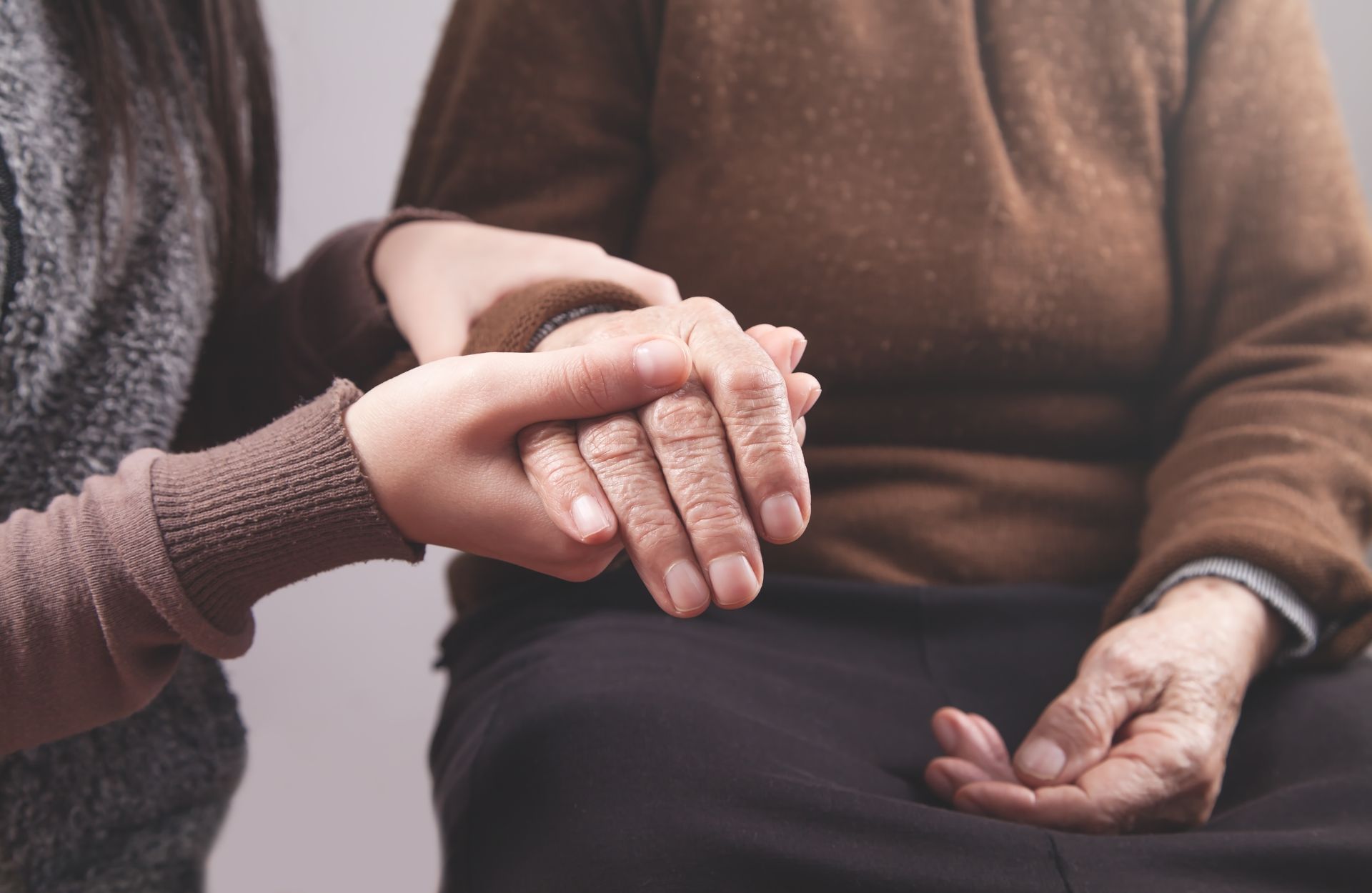 Person holding the hands of an elderly person, offering support and comfort.