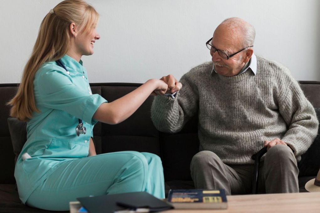 A nurse is giving an elderly man a high five while sitting on a couch.