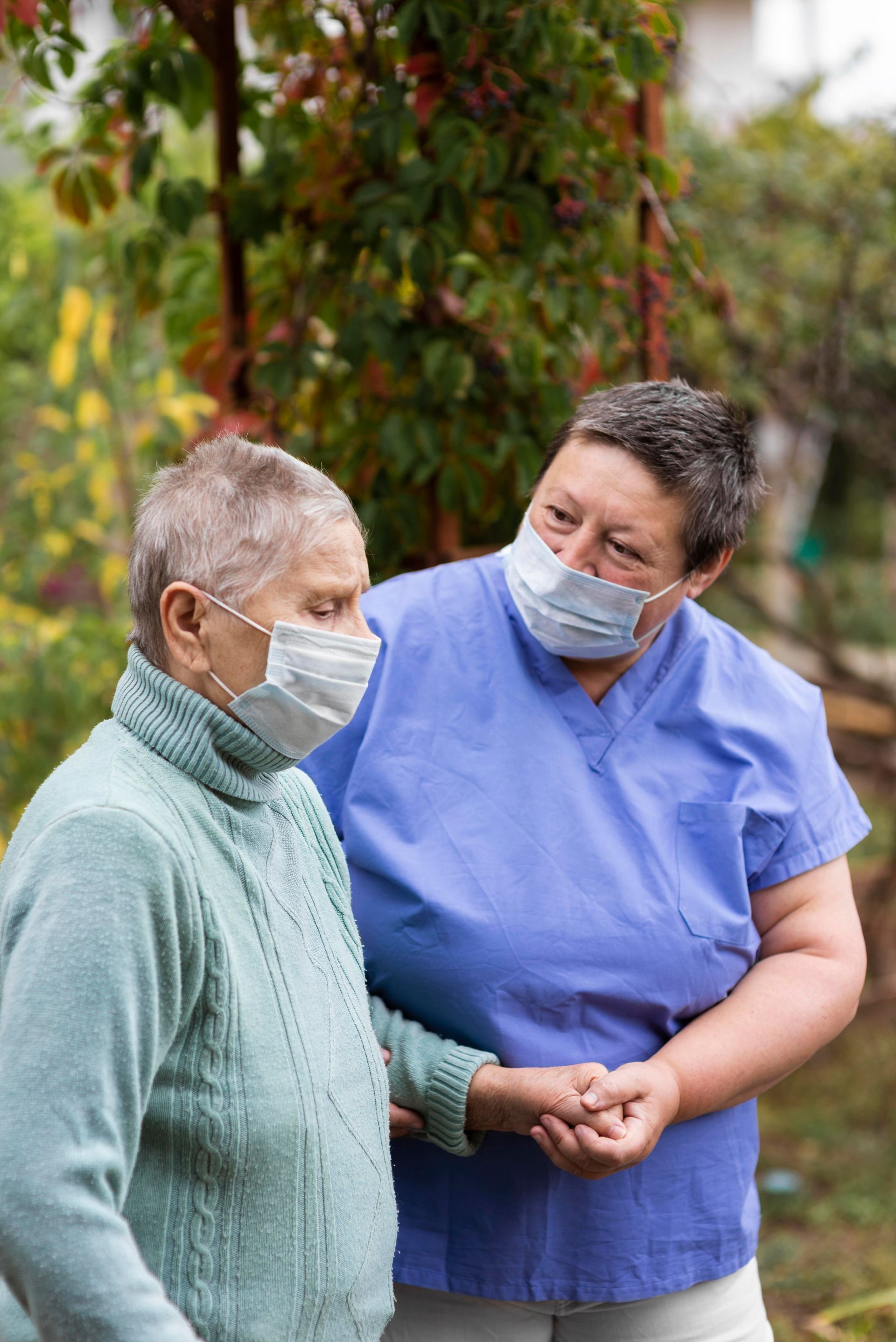 Person wearing mask comforts another masked person outdoors, holding their arm.