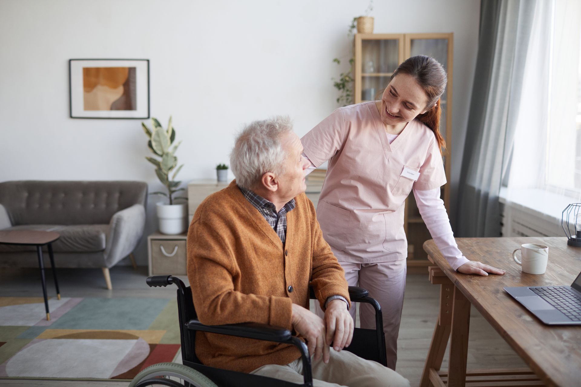 Caregiver talking with an elderly man in a wheelchair at home.