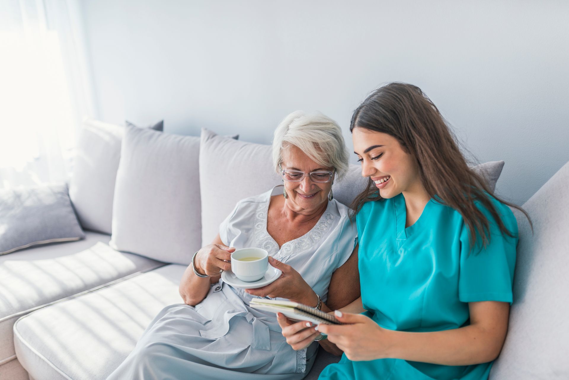 Nurse and elderly woman smiling while looking at a notebook on a couch.