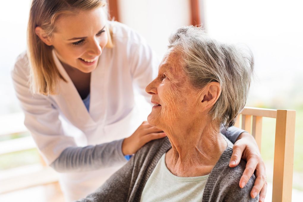 A nurse is talking to an elderly woman who is sitting in a chair.