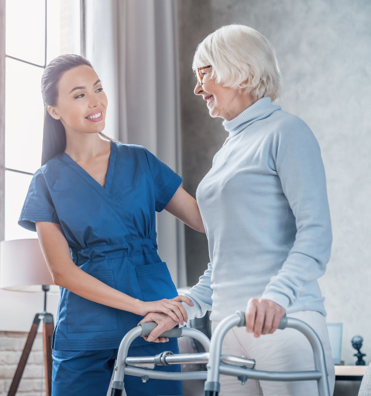 Caregiver assisting a person using a walker, smiling indoors.
