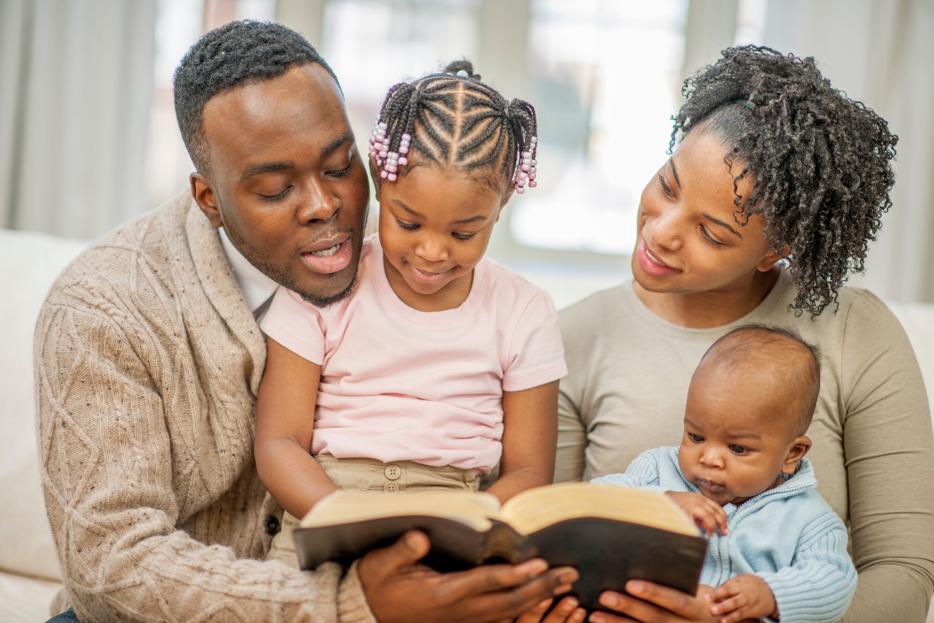 A family is sitting on a couch reading a bible together.
