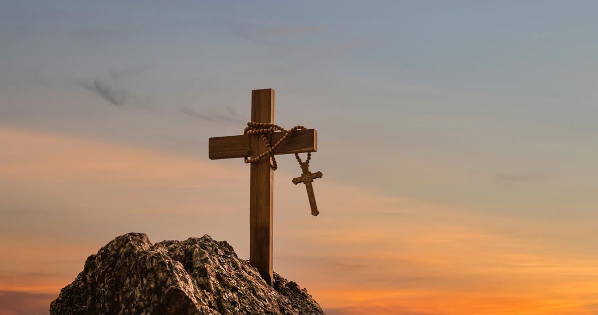 A wooden cross with a cross hanging from it is on top of a rock.