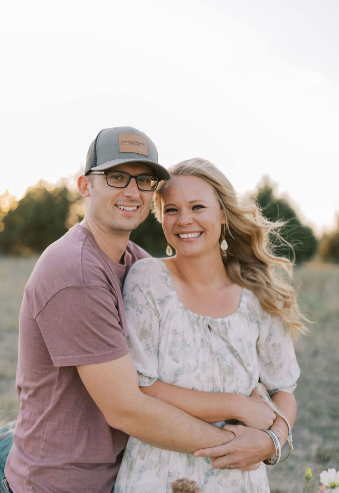 Two men in sunglasses smile at the camera, with a coastal vista and mountains in the background.
