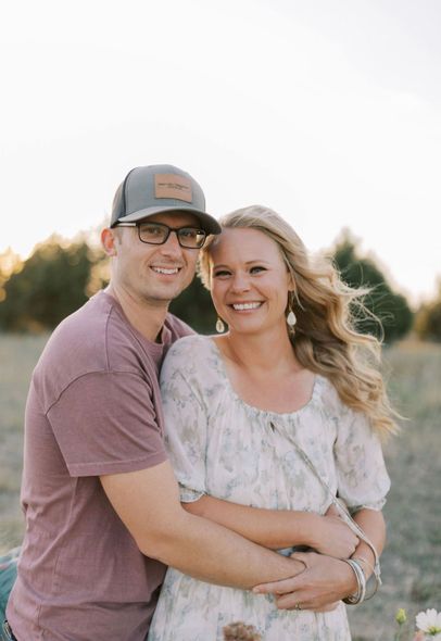 Two men in sunglasses smile at the camera, with a coastal vista and mountains in the background.