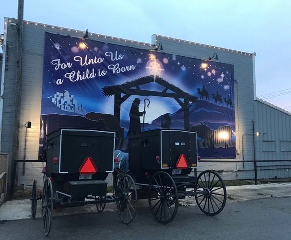 Two black horse-drawn buggies parked in front of a nativity scene mural on a building.