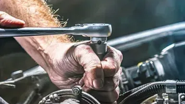 Hands using a wrench to work on a car engine in a garage.