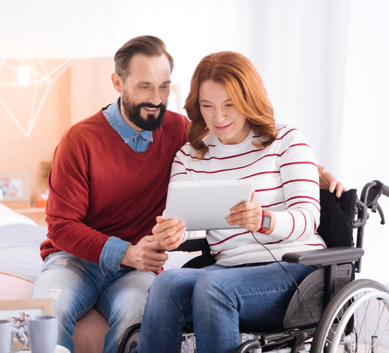 Relaxing together. Happy loving bearded man and disabled woman of middle age smiling and using a tablet while sitting