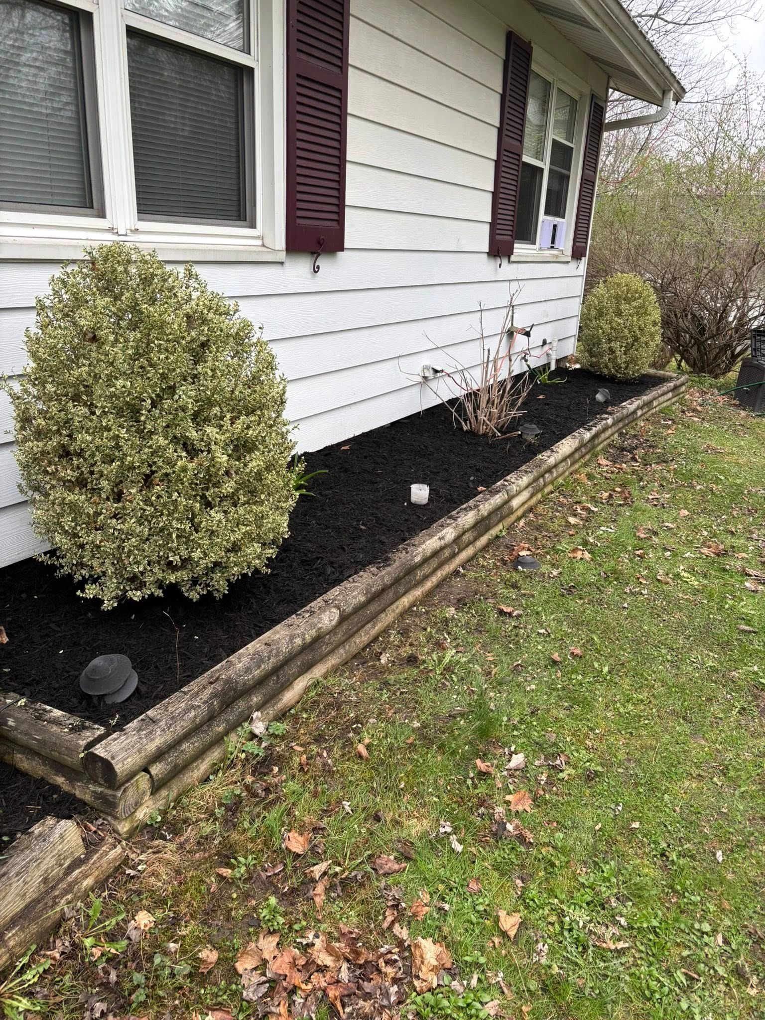 White house with a mulch-covered flower bed bordered by aged wood.