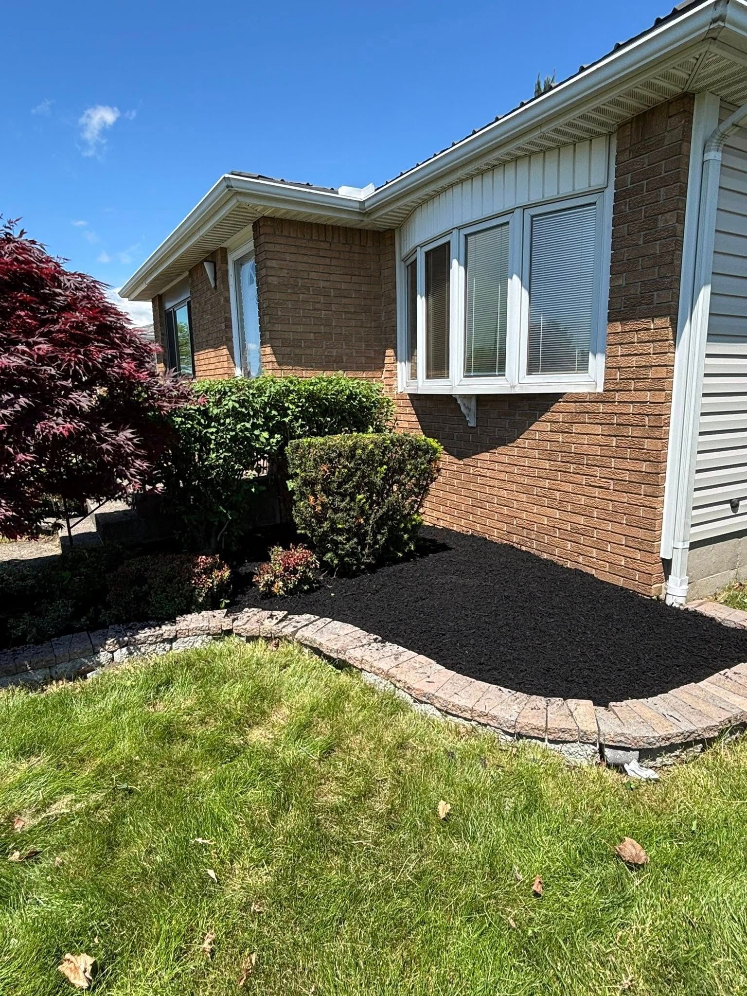 Brick house with mulched flowerbed, green lawn, and sunny blue sky.
