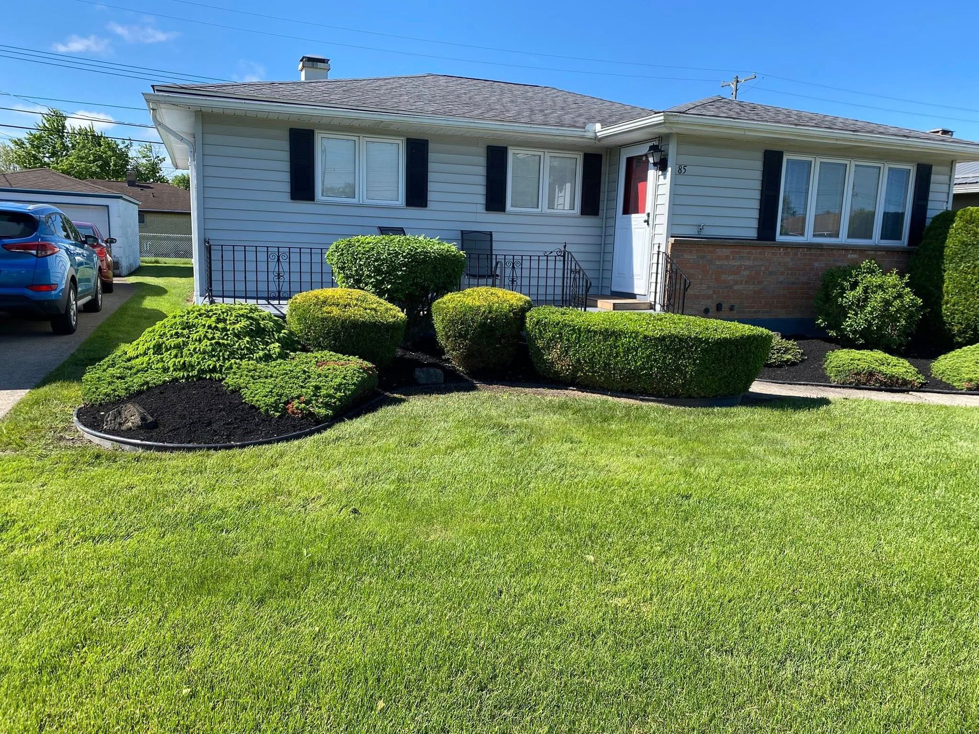 Light blue house with manicured hedges, green lawn, and blue car parked in the driveway.