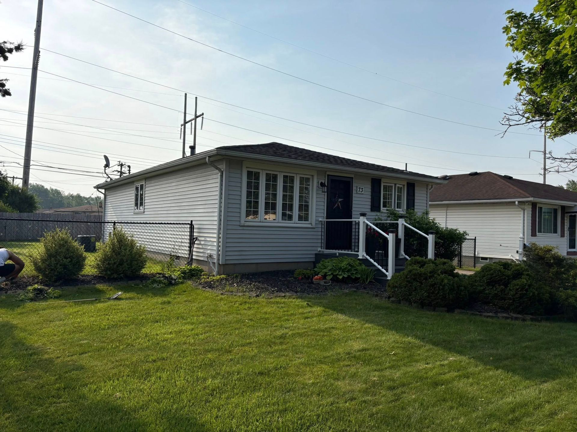 Gray suburban bungalow house with grass lawn and front garden, sunny day.