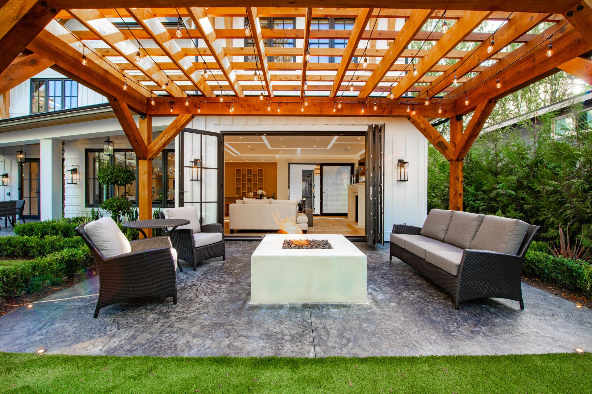 Outdoor patio with a wooden pergola, seating around a fire pit, and a house in the background.