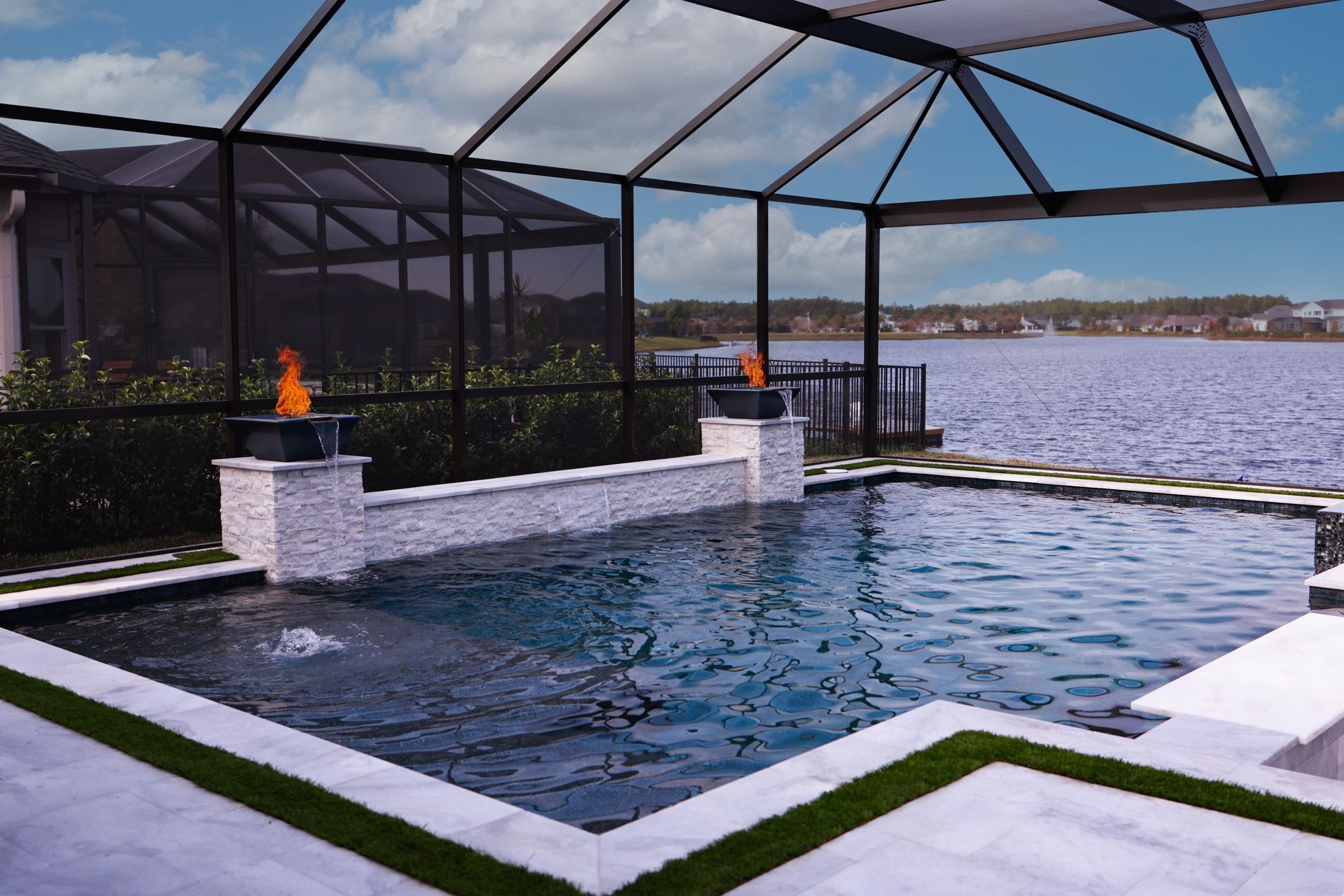 Pool with dark tile, reflecting sunset and view of a lake and homes.