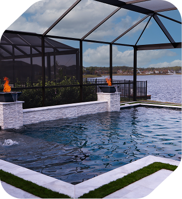 A screened-in pool patio featuring a stone wall with two glowing fire bowls overlooking a lake.