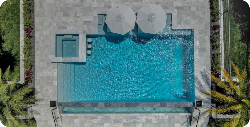 Infinity pool overlooking a body of water with docks, white umbrellas, and a cloudy sky.