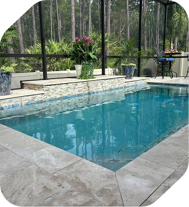 A clear, rectangular swimming pool surrounded by stone pavers, featuring a tiled raised wall with potted plants.
