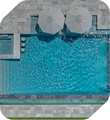 Top-down view of a rectangular, bright blue swimming pool with a hot tub, tiled deck, and two grey patio umbrellas.