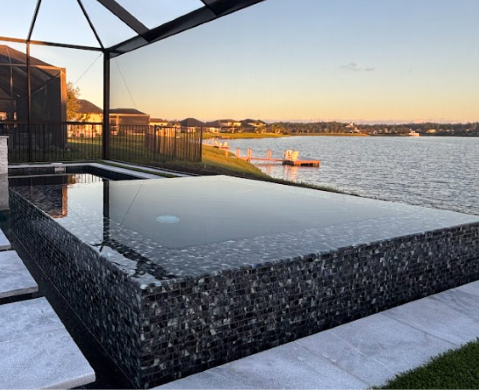 Overhead view of a rectangular turquoise pool with a jacuzzi, umbrellas, and stone patio.