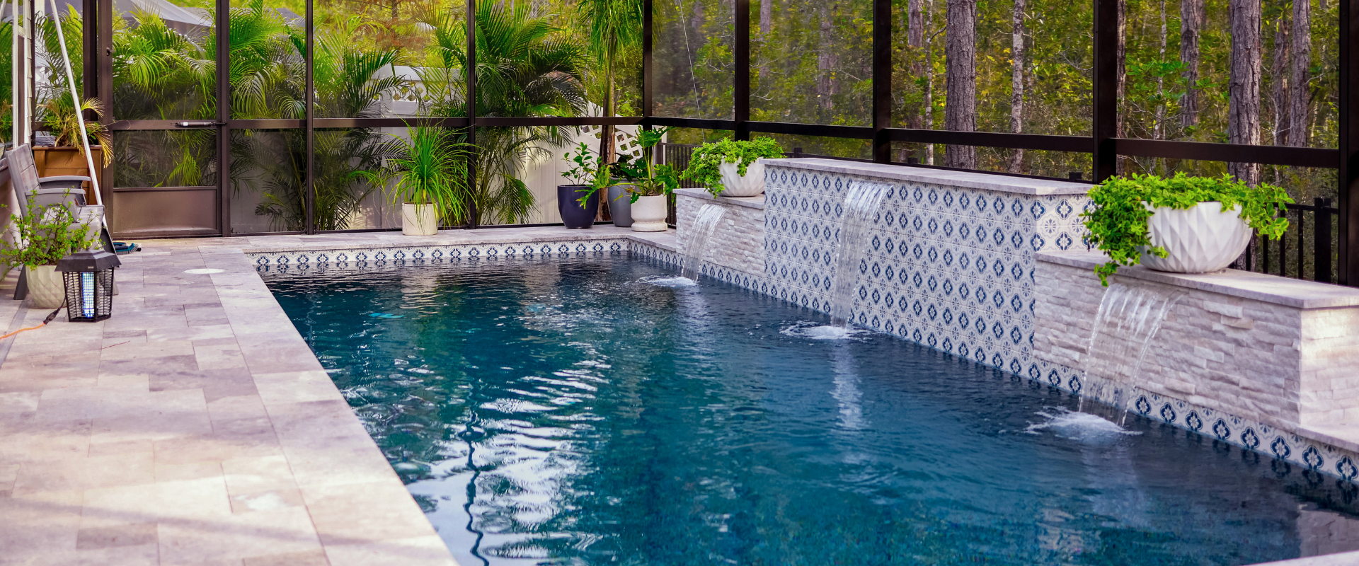A rectangular swimming pool with tiled water features and fountains under a screened enclosure surrounded by greenery.