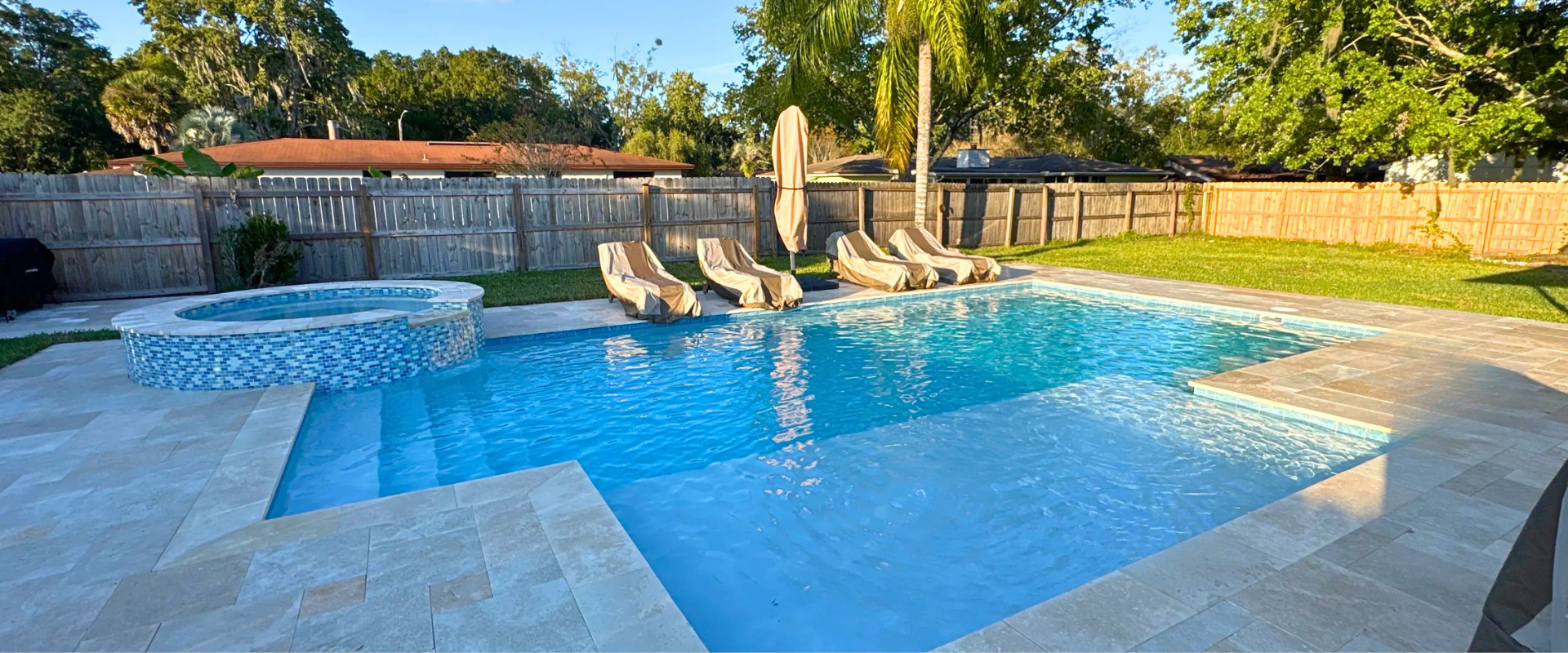 Backyard swimming pool with stone deck, waterfall spa, and lounge chairs in warm sunlight