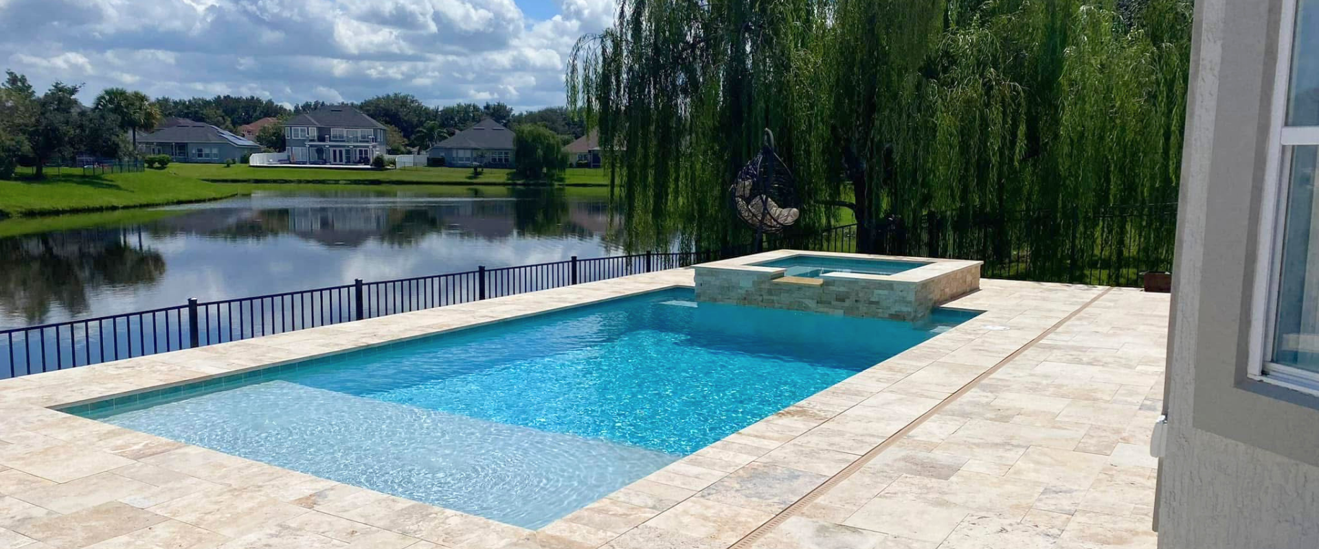 Modern backyard pool beside a lake, with blue water and a raised hot tub on a stone patio