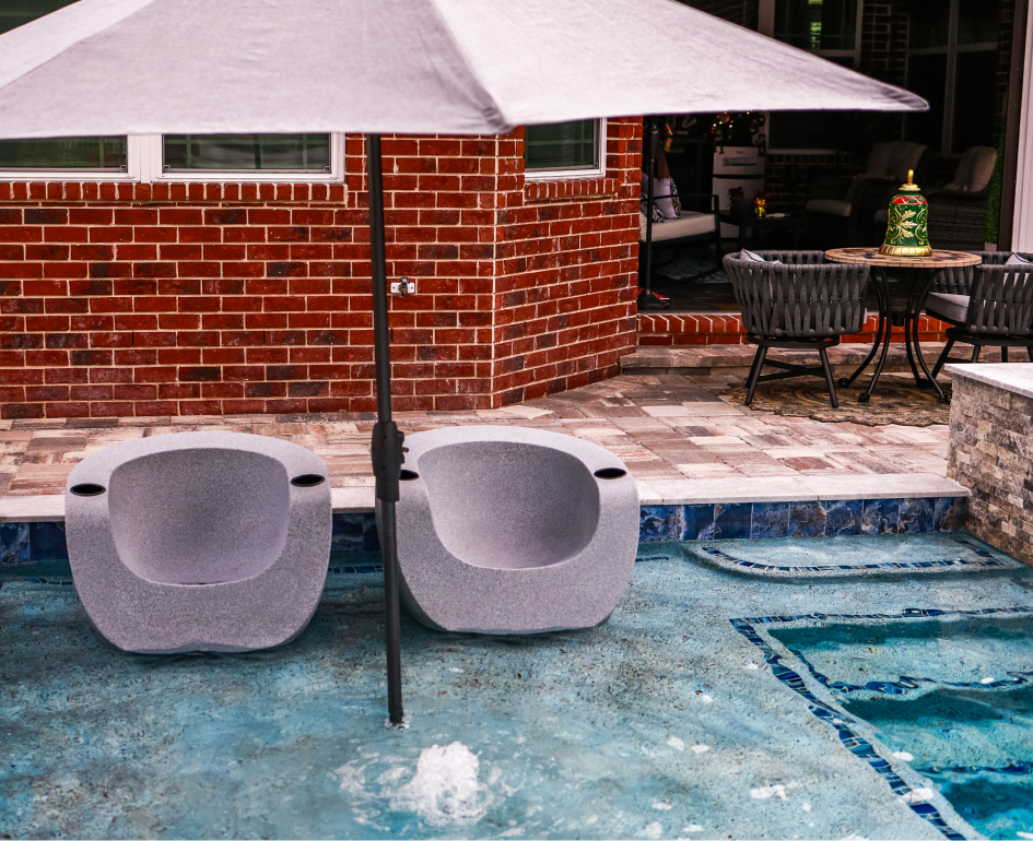 Overhead view of a rectangular turquoise pool with a jacuzzi, umbrellas, and stone patio.