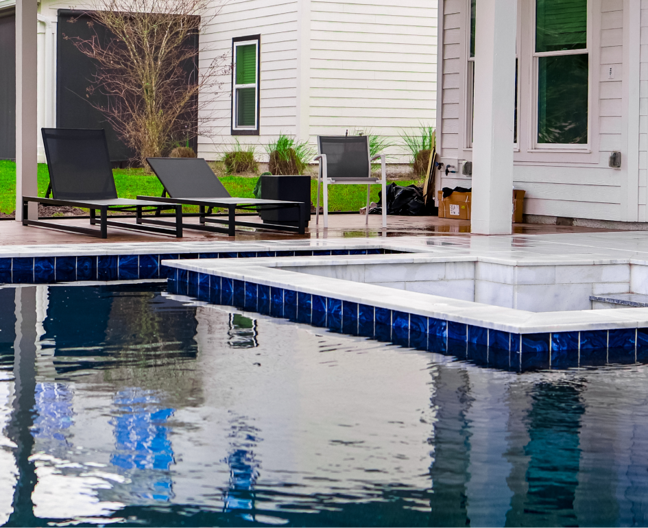 Overhead view of a rectangular turquoise pool with a jacuzzi, umbrellas, and stone patio.