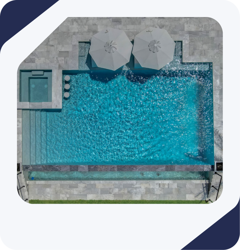 Overhead view of a rectangular turquoise pool with a jacuzzi, umbrellas, and stone patio.