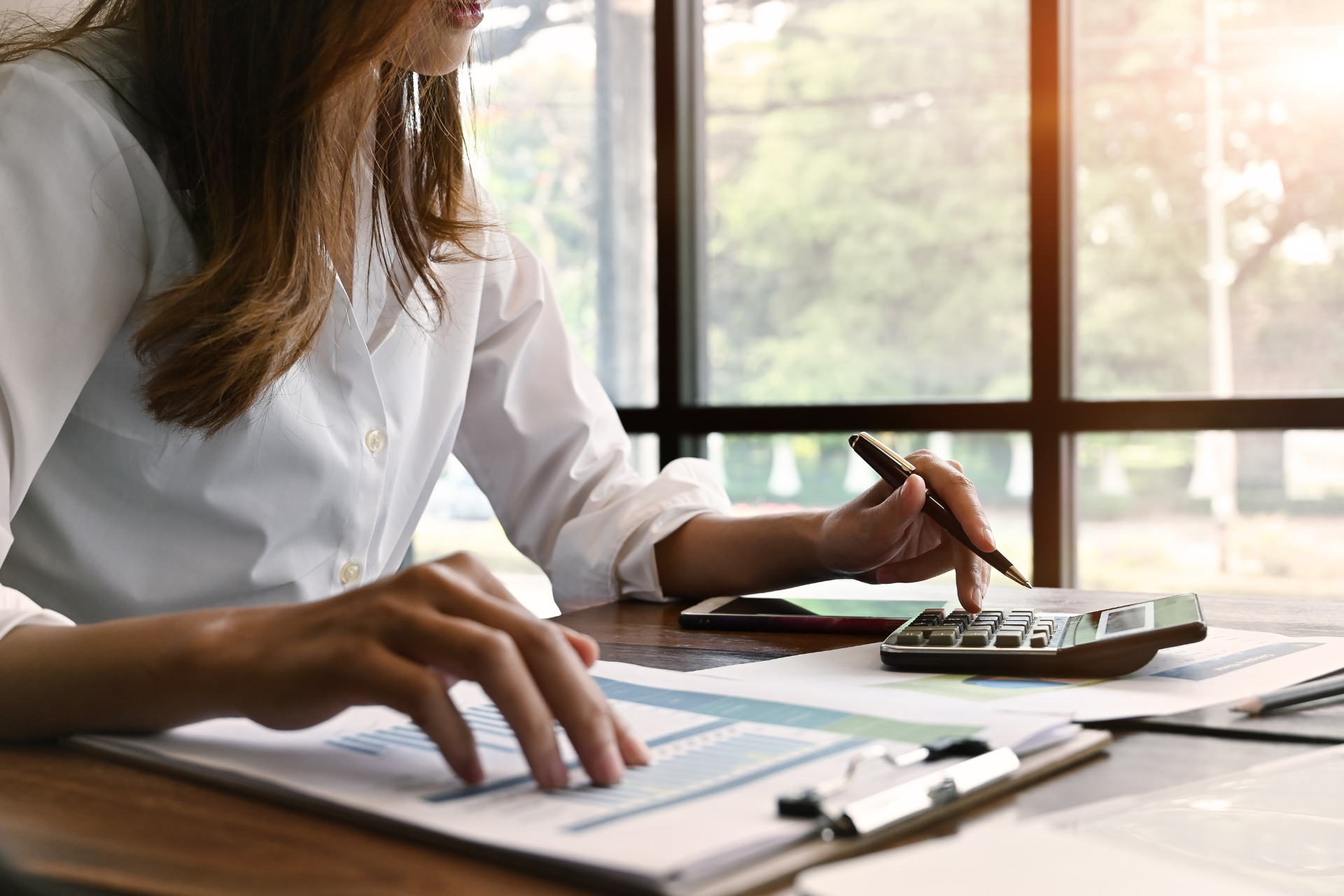 A woman is sitting at a desk using a calculator and a pen.