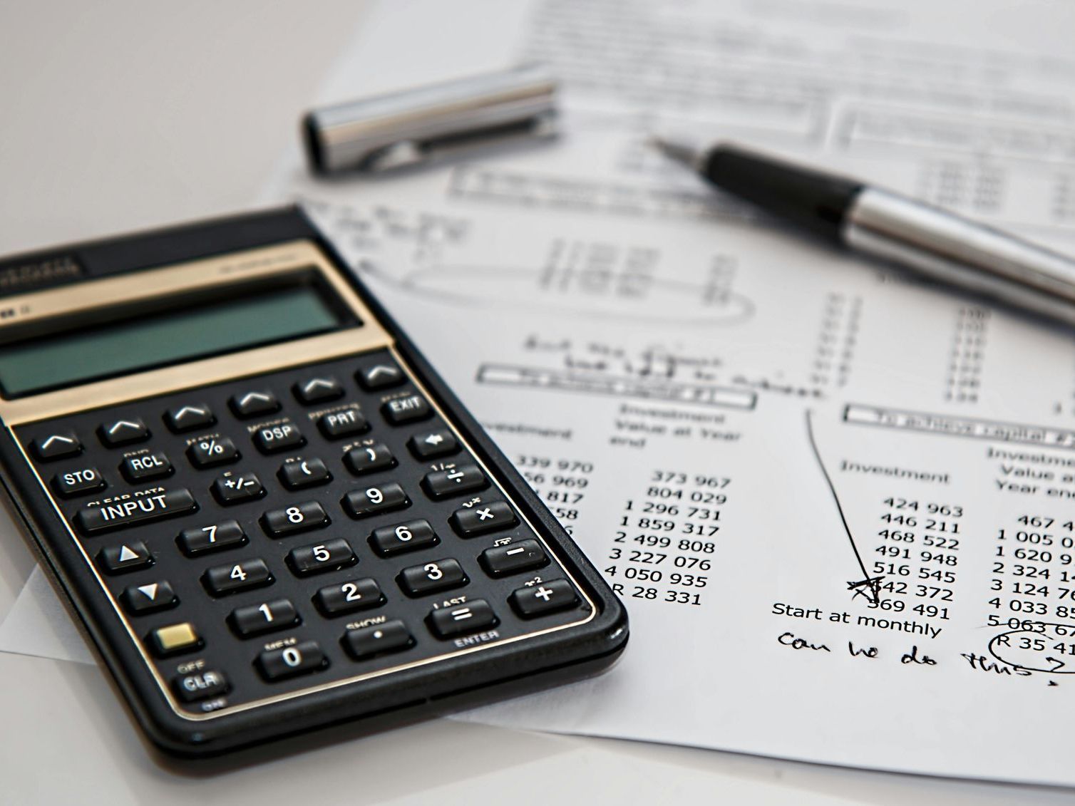 A calculator sits on top of a piece of paper next to a pen