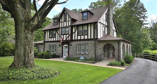 A large house with a driveway leading to it is surrounded by trees.