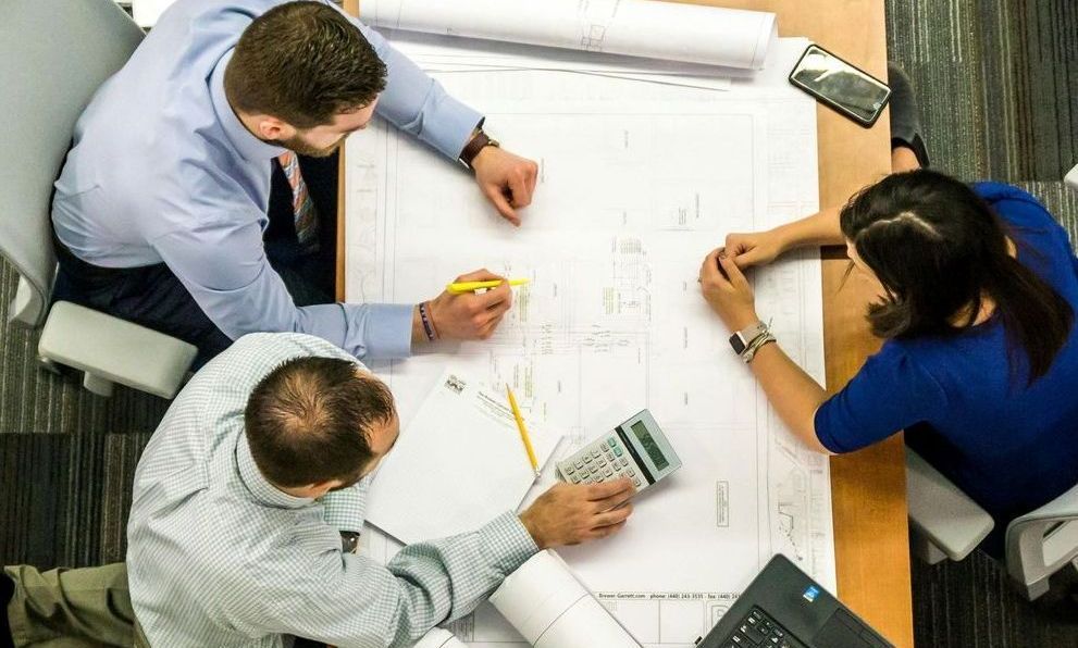 A group of people are sitting around a table looking at a blueprint.