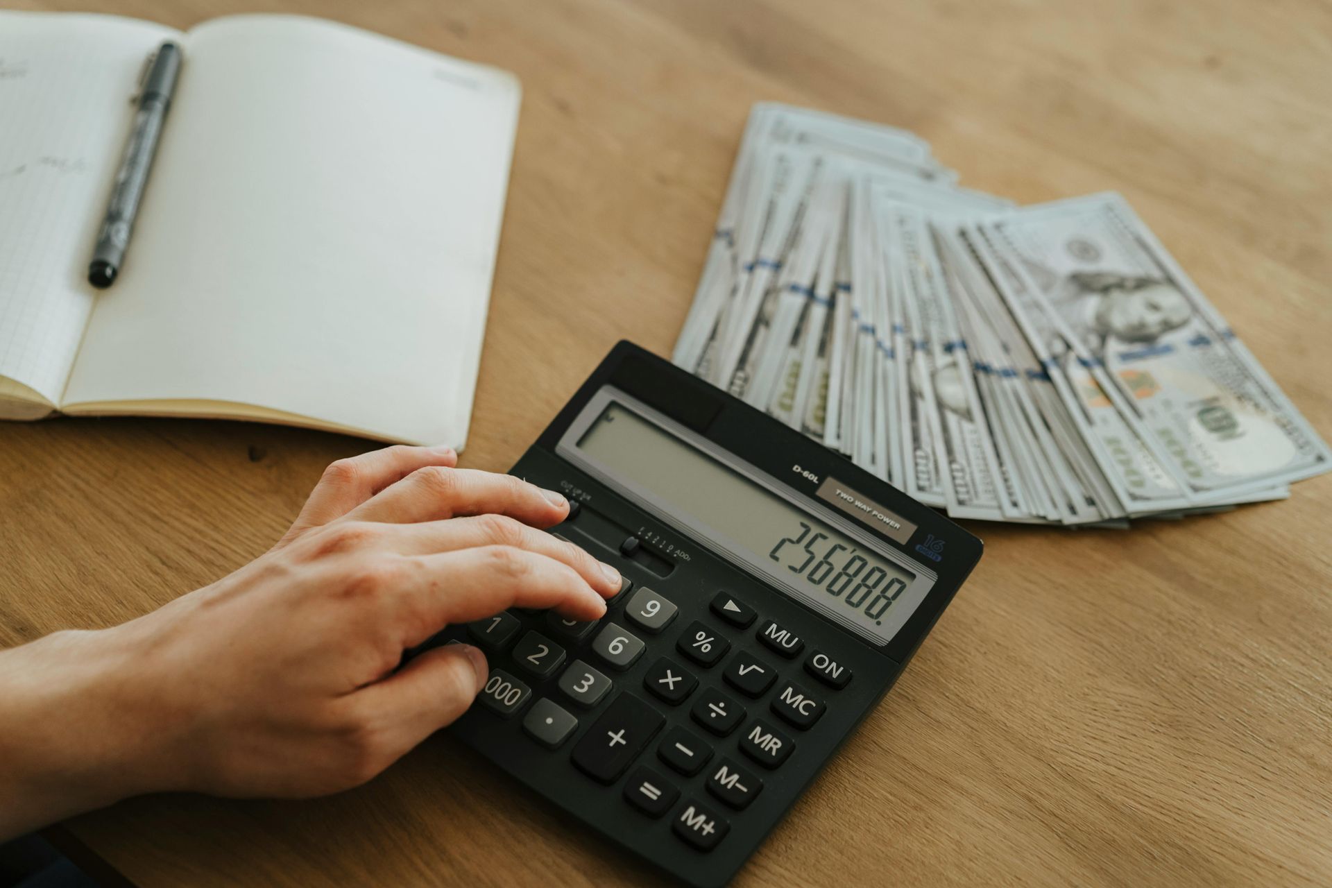 A person is using a calculator next to a pile of money.