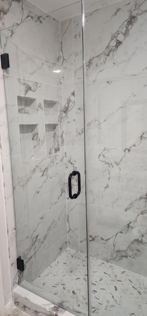 A shower stall with a marble wall and a glass door.