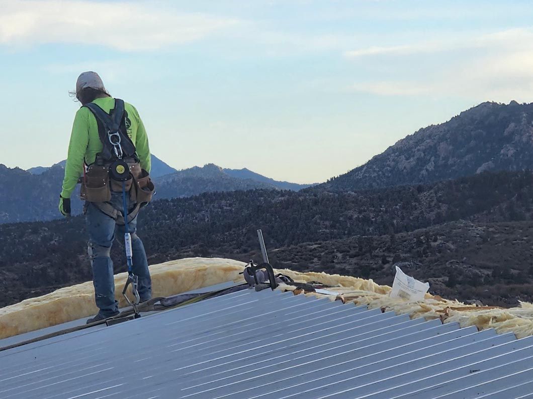 A man is standing on top of a metal roof with mountains in the background.