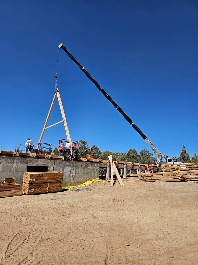 A crane is lifting a wooden structure in a dirt field.