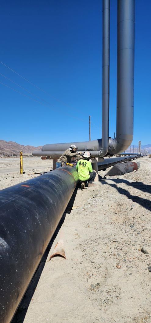 A man is standing next to a large pipe in the desert.