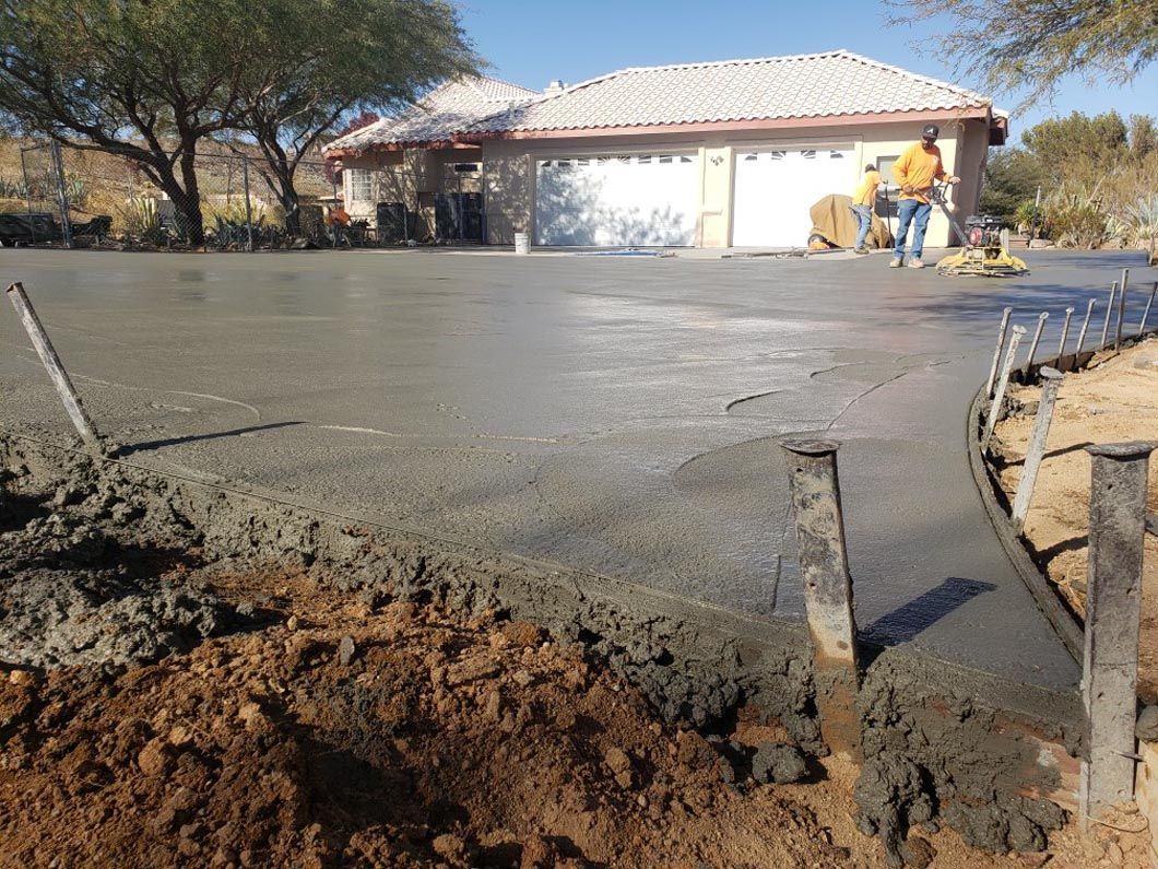 A man is pouring concrete into a driveway in front of a house.