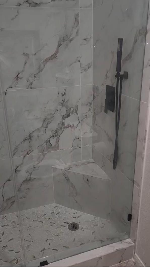 A bathroom with a walk in shower with marble tiles and a glass door.