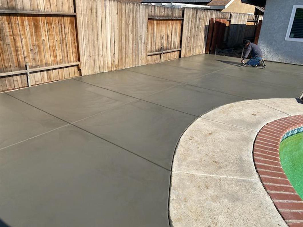 A man is kneeling on a concrete patio next to a pool.