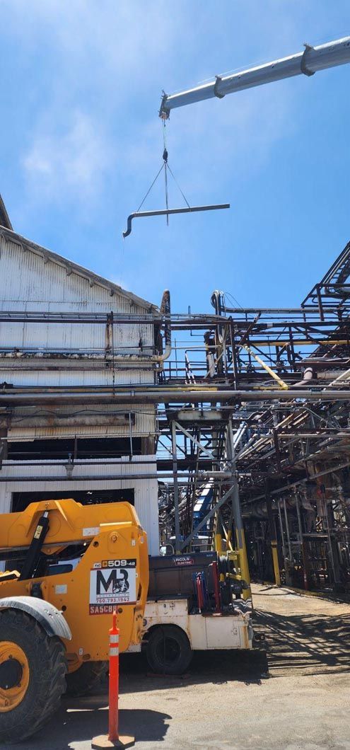 A crane is lifting a pipe in front of a building.