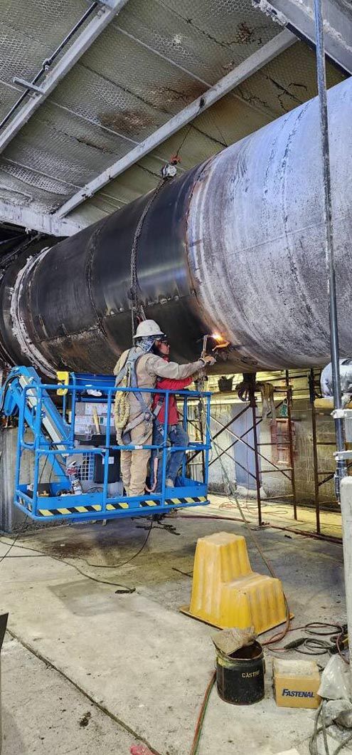 Two men are welding a large pipe in a factory.