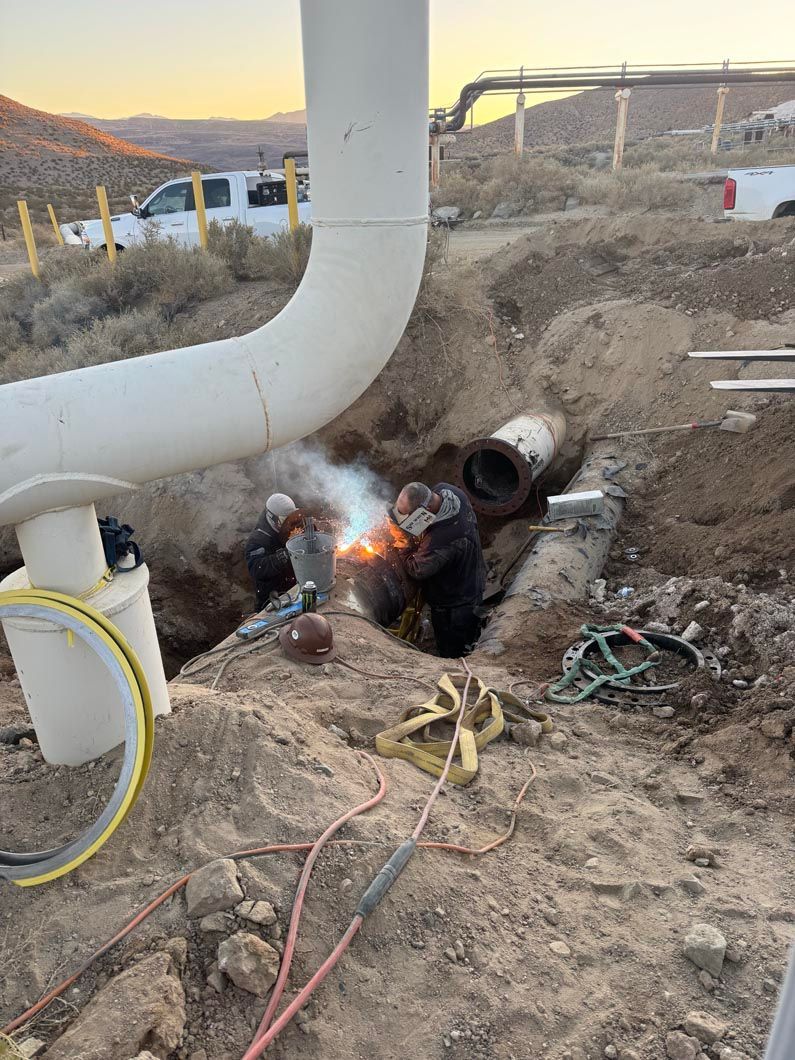 A man is welding a pipe in a hole in the ground.