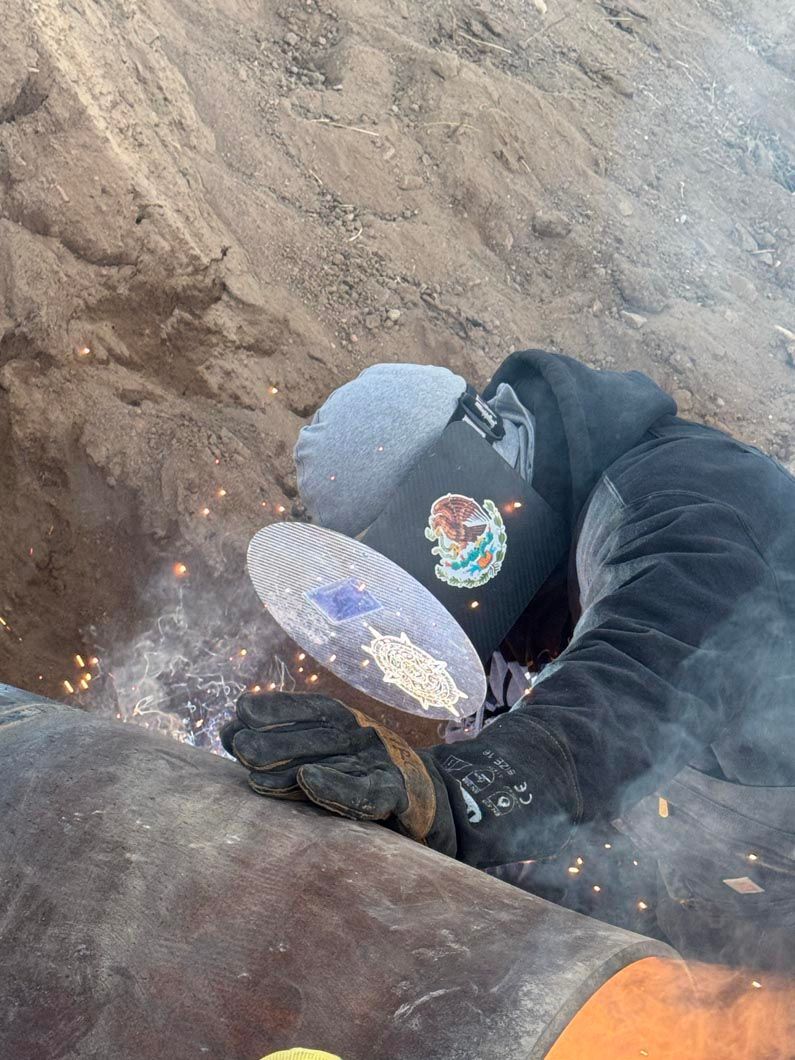 A man is welding a pipe in the dirt.