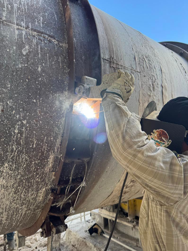A man is welding a large pipe on a construction site.