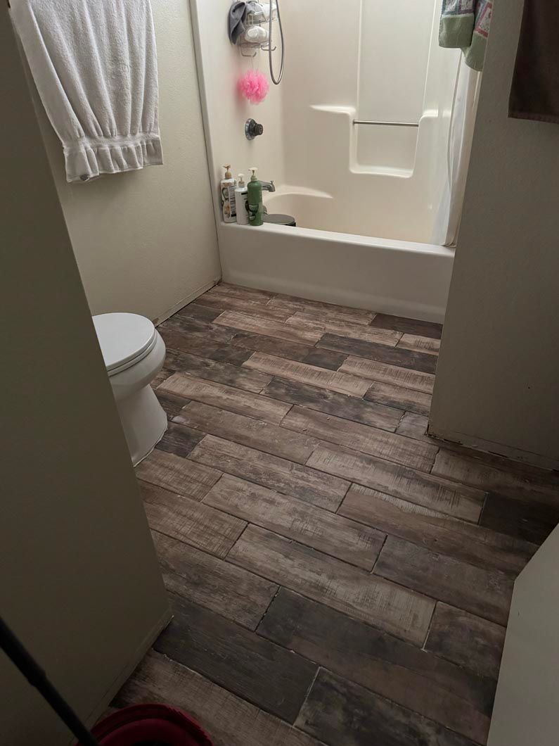 A bathroom with a toilet , tub , shower and wooden floor.